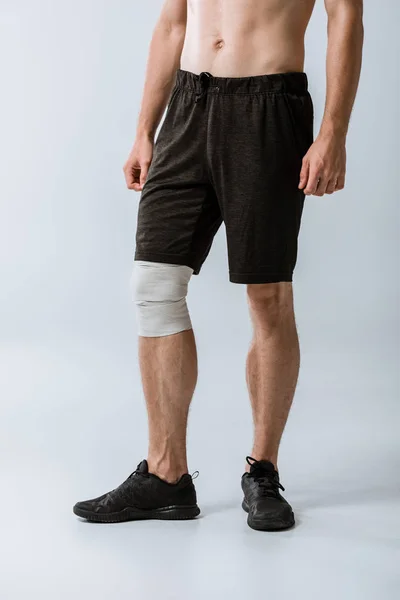 Cropped view of sportsman with elastic bandage on knee on grey — Stock Photo