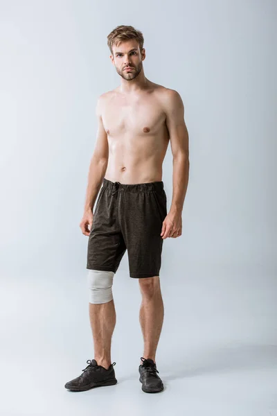 Vue pleine longueur du sportif torse nu avec bandage élastique sur le genou sur gris — Photo de stock