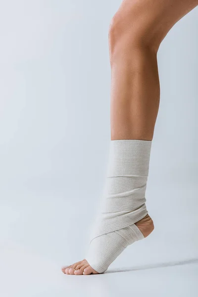 Partial view of barefoot girl with elastic bandage on foot on grey — Stock Photo