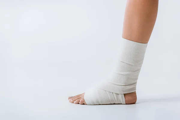 Partial view of barefoot girl with elastic bandage on foot on grey — Stock Photo