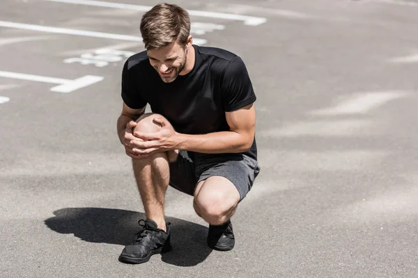 Deportista barbudo en camiseta negra con dolor de rodilla en la calle - foto de stock