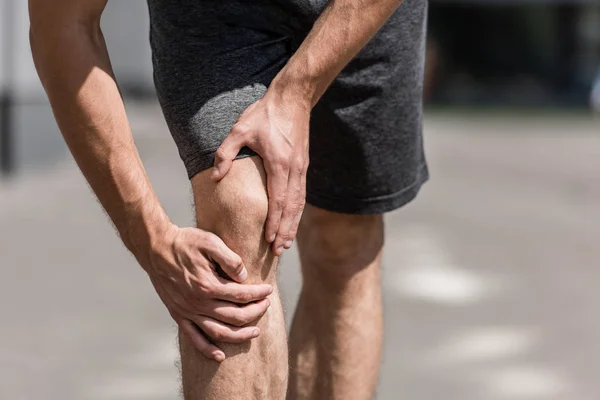 Partial view of sportsman with knee pain on street — Stock Photo