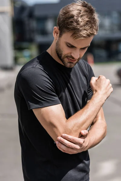 Sportsman in black t-shirt with elbow pain on street — Stock Photo