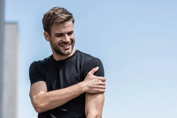 Deportista en camiseta negra con dolor de hombro bajo el cielo azul - foto de stock