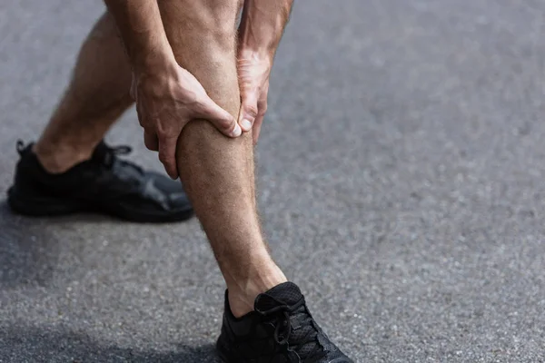 Vista parcial del deportista en zapatillas negras con dolor en las piernas en la calle - foto de stock