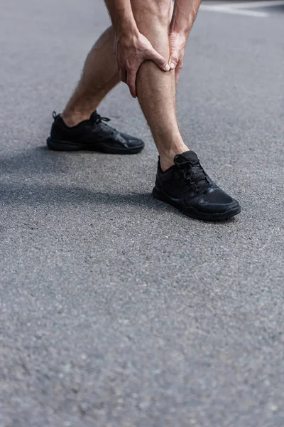 Partial view of sportsman in black sneakers with leg pain on street — Stock Photo