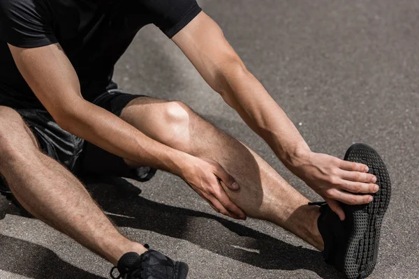 Cropped view of sportsman with leg injury on street — Stock Photo