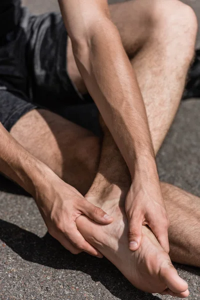 Vista parcial del deportista descalzo con dolor en el pie en la calle - foto de stock