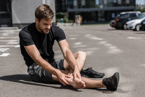 Muscular bearded barefoot sportsman with foot pain on street — Stock Photo