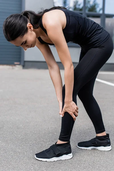 Ganzkörperansicht einer Sportlerin mit Beinschmerzen auf der Straße — Stockfoto