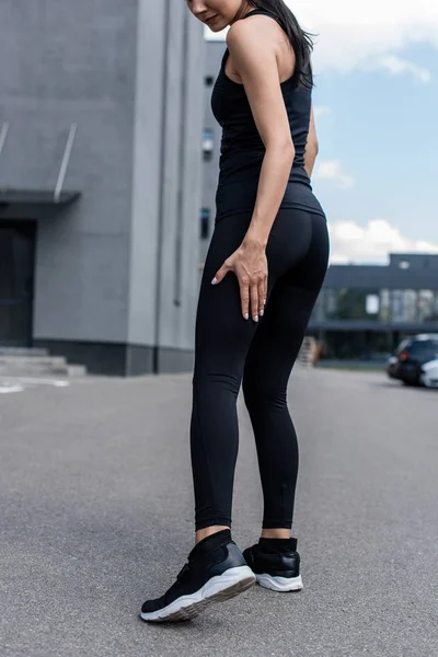 Vista ritagliata di sportiva in scarpe da ginnastica nere sulla strada — Foto stock