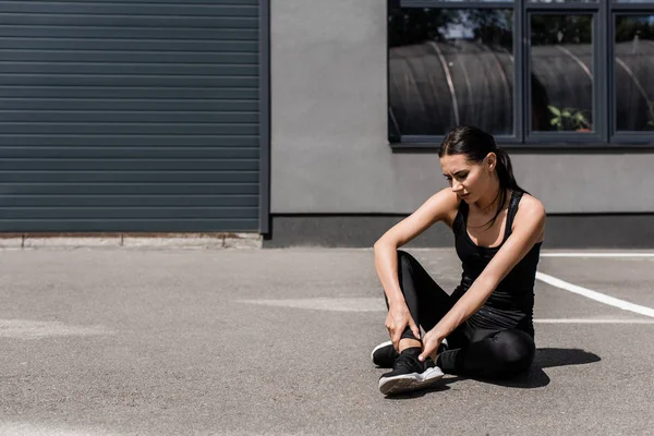 Sportlerin in schwarzen Turnschuhen mit Knöchelschmerzen auf der Straße — Stockfoto