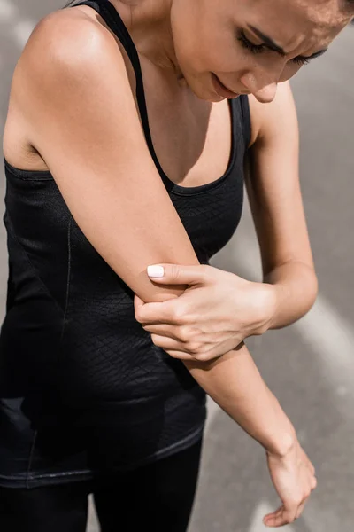 Cropped view of sportswoman with elbow pain on street in sunny day — Stock Photo