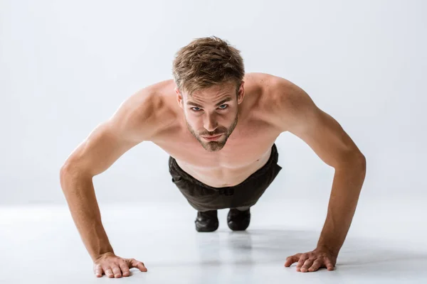 Front view of sportsman doing push ups and looking at camera on grey — Stock Photo