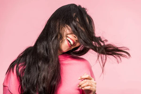 Mulher em pulôver rosa sorrindo e brincando com o cabelo isolado em rosa — Fotografia de Stock