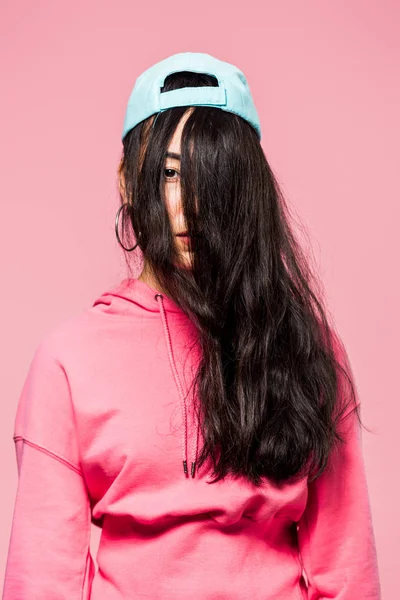 Atraente asiático mulher no rosa pulôver e cap olhando para câmera isolado no rosa — Fotografia de Stock