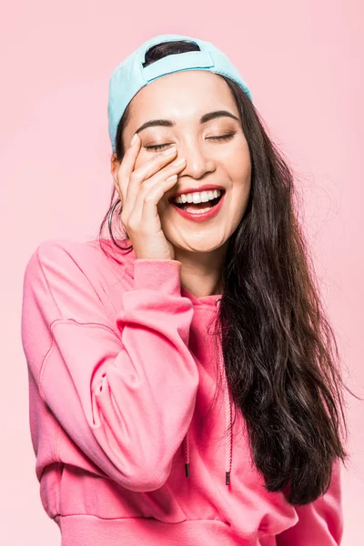 Attrayant asiatique femme avec les yeux fermés en rose pullover et chapeau sourire isolé sur rose — Photo de stock