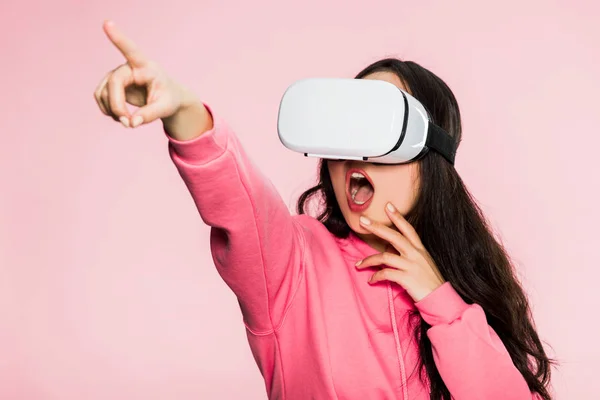 Shocked woman in pink pullover with virtual reality headset pointing with finger isolated on pink — Stock Photo