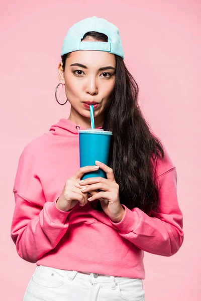 Atraente asiático mulher no pulôver e cap beber de plástico copo isolado no rosa — Fotografia de Stock