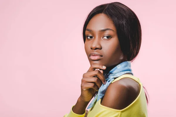 Atractiva mujer afroamericana en bufanda azul mirando a la cámara aislada en rosa - foto de stock