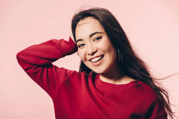 Atractivo asiático mujer en rojo suéter sonriendo aislado en rosa - foto de stock