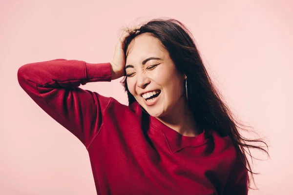 Приваблива азіатська жінка в червоному светрі з закритими очима посміхається ізольовано на рожевому — стокове фото