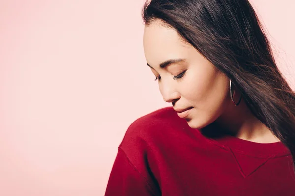 Atractiva mujer asiática en suéter rojo con los ojos cerrados aislados en rosa - foto de stock