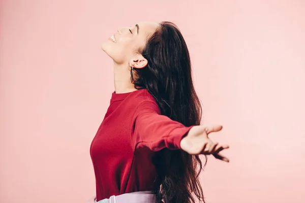 Side view of attractive asian woman with outstretched hands in red sweater smiling isolated on pink — Stock Photo