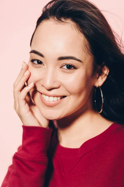 Atractivo asiático mujer en rojo suéter sonriendo aislado en rosa - foto de stock