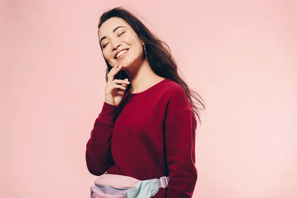 Attraktive asiatische Frau mit geschlossenen Augen in rotem Pullover, die isoliert auf rosa lächelt — Stockfoto