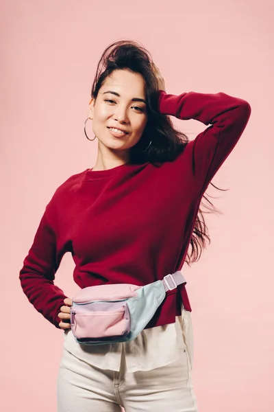 Attraktive asiatische Frau im roten Pullover lächelt isoliert auf rosa — Stockfoto