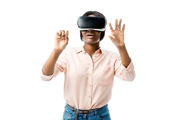 Femme afro-américaine choquée en chemise avec casque de réalité virtuelle montrant les mains isolées sur blanc — Photo de stock