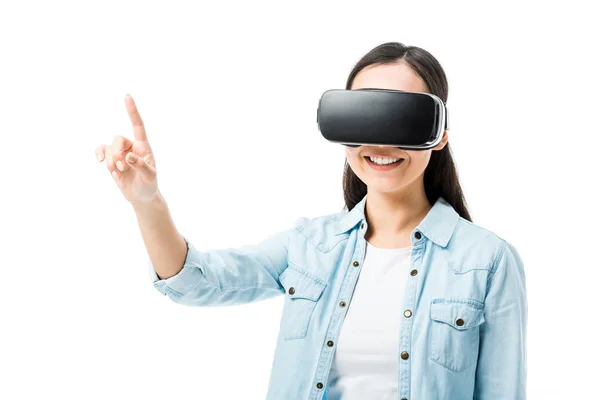 Donna sorridente in camicia di jeans con auricolare realtà virtuale che punta con dito isolato su bianco — Foto stock