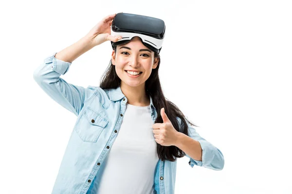 Mujer asiática en camisa vaquera con auriculares de realidad virtual mostrando el pulgar hacia arriba aislado en blanco - foto de stock