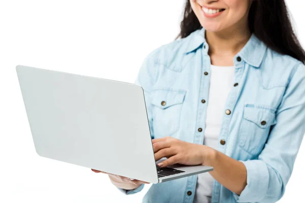 Vista recortada de la mujer en camisa de mezclilla sonriendo y sosteniendo portátil aislado en blanco - foto de stock