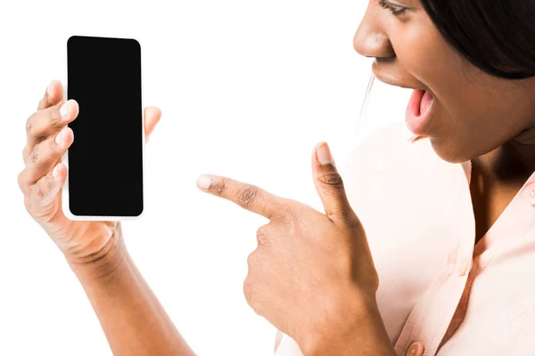 Femme afro-américaine choquée en chemise pointant du doigt le smartphone isolé sur blanc — Photo de stock