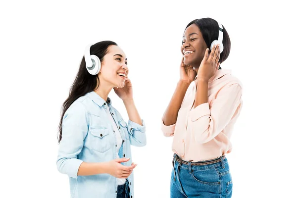 Smiling asian and african american friends listening music in headphones isolated on white — Stock Photo