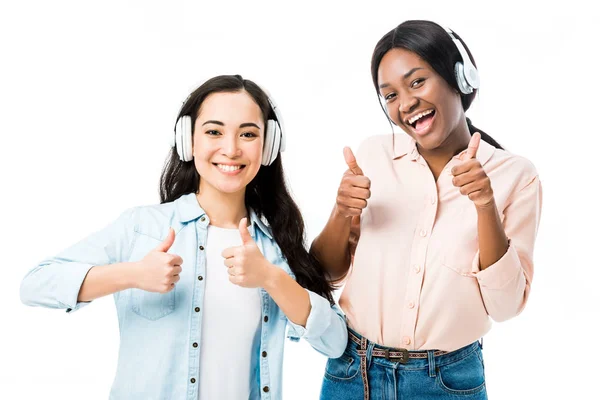 Sonriente asiático y africano americano amigos en auriculares mostrando pulgares arriba aislado en blanco - foto de stock