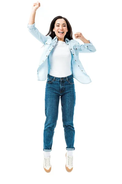 Приваблива і усміхнена азіатська жінка в джинсовій сорочці стрибає і показує так жест ізольовано на білому — стокове фото