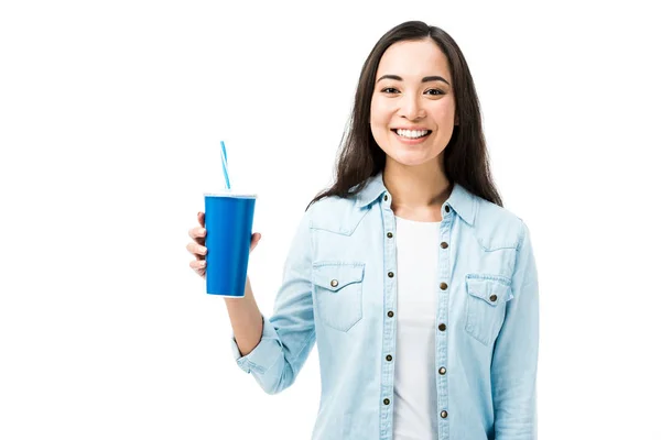 Atractiva y sonriente mujer asiática en camisa de mezclilla sosteniendo taza de plástico aislado en blanco - foto de stock