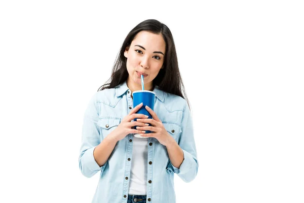 Приваблива азіатська жінка в джинсовій сорочці, що п'є з пластикової чашки, ізольована на білому — стокове фото