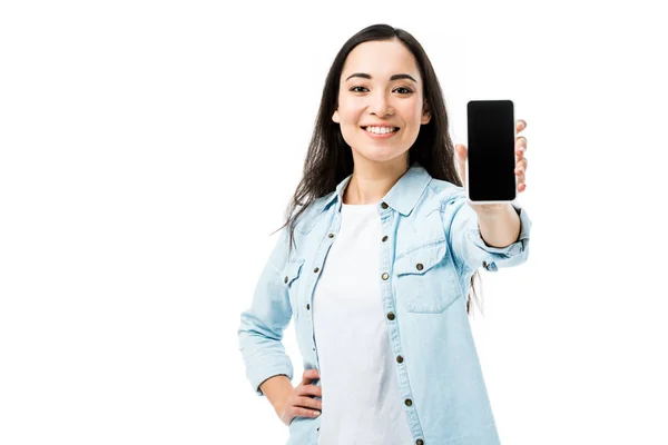 Atractiva y sonriente mujer asiática en camisa de mezclilla sosteniendo teléfono inteligente con espacio de copia aislado en blanco - foto de stock