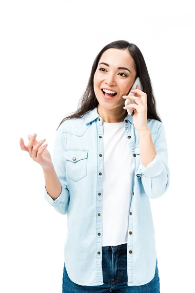 Attractive and smiling asian woman in denim shirt talking on smartphone isolated on white — Stock Photo