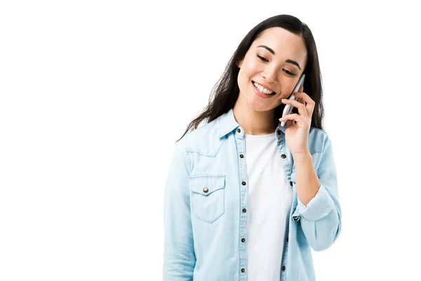 Atractiva y sonriente mujer asiática en camisa de mezclilla hablando en teléfono inteligente aislado en blanco - foto de stock
