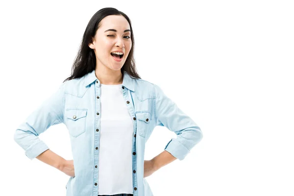 Attraktive und lächelnde asiatische Frau im Jeanshemd zwinkert vereinzelt auf weißem Grund — Stockfoto
