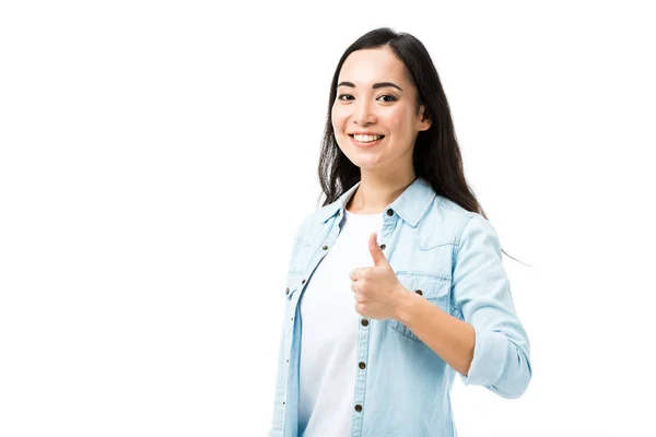 Atractivo y sonriente asiático mujer en denim camisa mostrando pulgar hacia arriba aislado en blanco - foto de stock