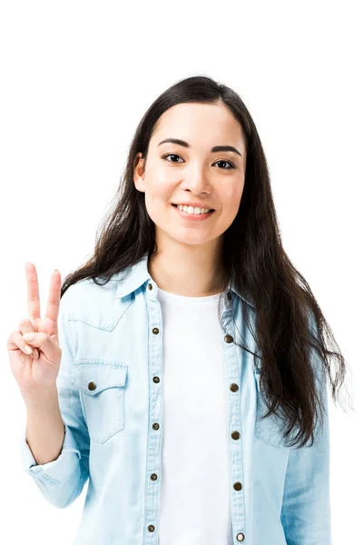 Atractivo y sonriente asiático mujer en denim camisa mostrando paz signo aislado en blanco - foto de stock
