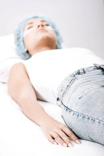 Selective focus of model in hair cap lying on couch isolated on grey — Stock Photo