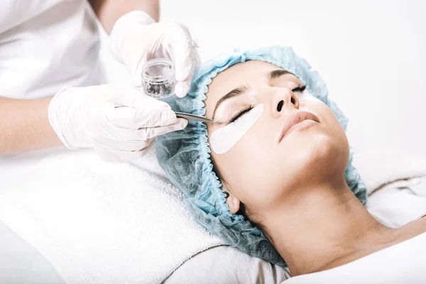 Eyelash master putting false eyelashes with tweezers on model face isolated on white — Stock Photo