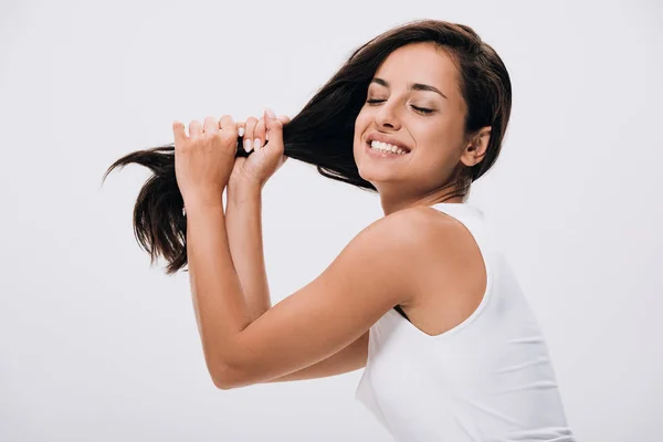 Feliz morena bela mulher segurando longo cabelo saudável e brilhante isolado no cinza — Fotografia de Stock